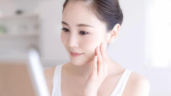 Young woman looking at the mirror happy after using Bepanthen Derma products